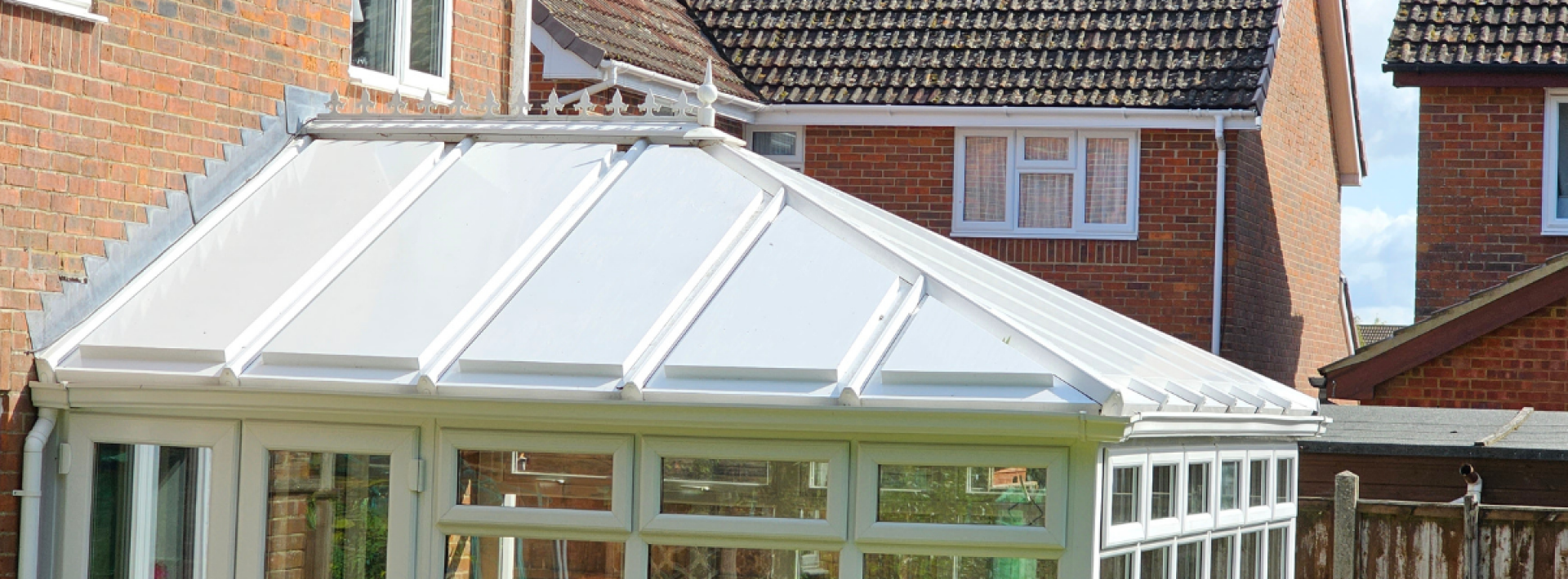 A Green Space UK conservatory roof with white panels in a flowery garden